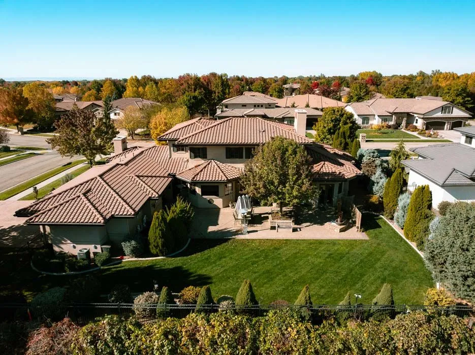 Aerial view of a large, brown-tiled roof house with a green lawn and autumn trees in a suburban setting.