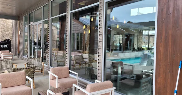 Outdoor patio with seating and large glass windows reflecting a pool and interior space.