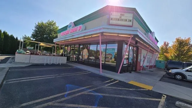 Exterior of a pink and green diner with a drive-in window under a sunny sky.