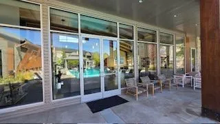 Exterior of a building with glass windows and doors; pool visible through the glass.