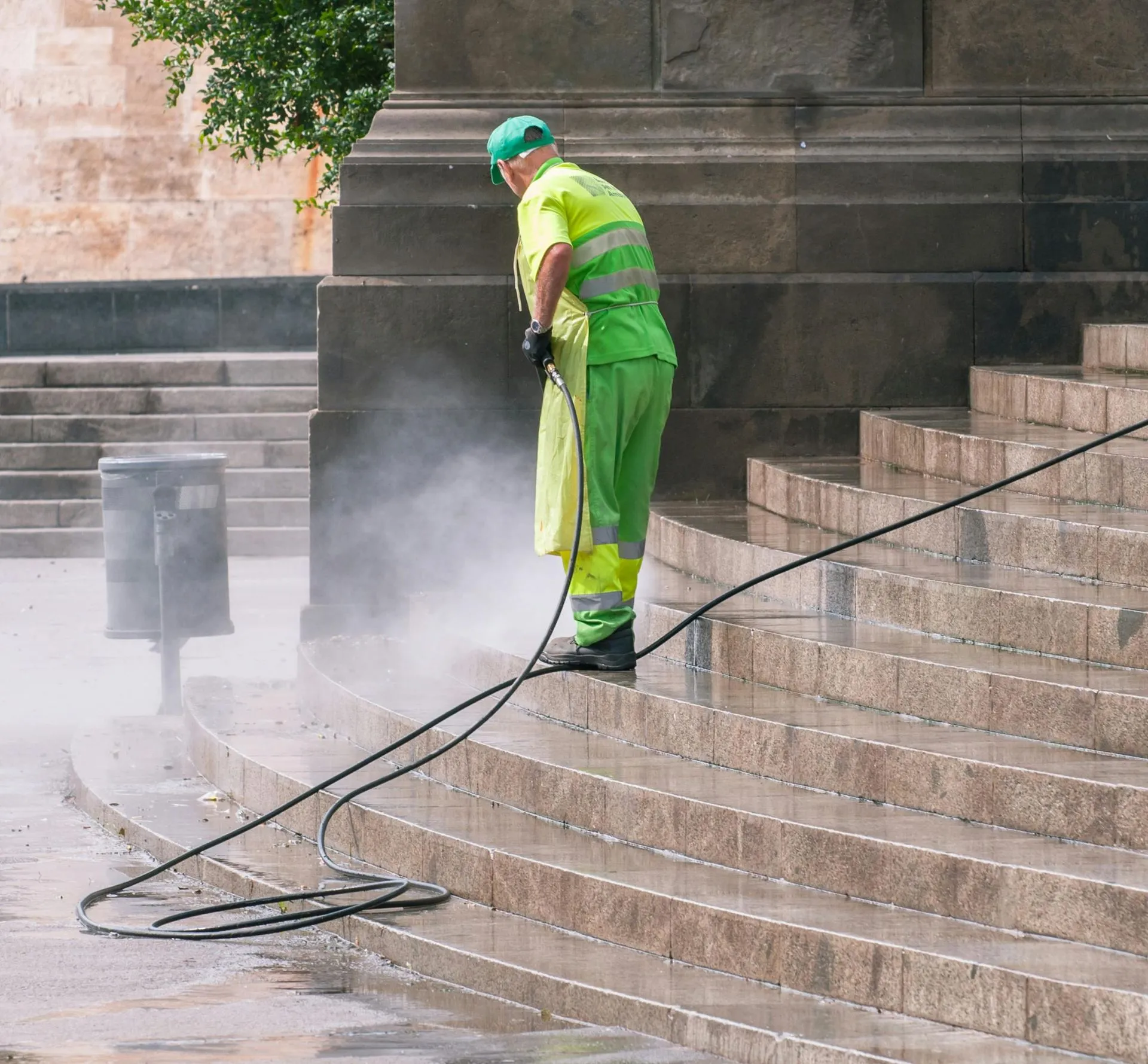 Man in green uniform power washing stone steps.