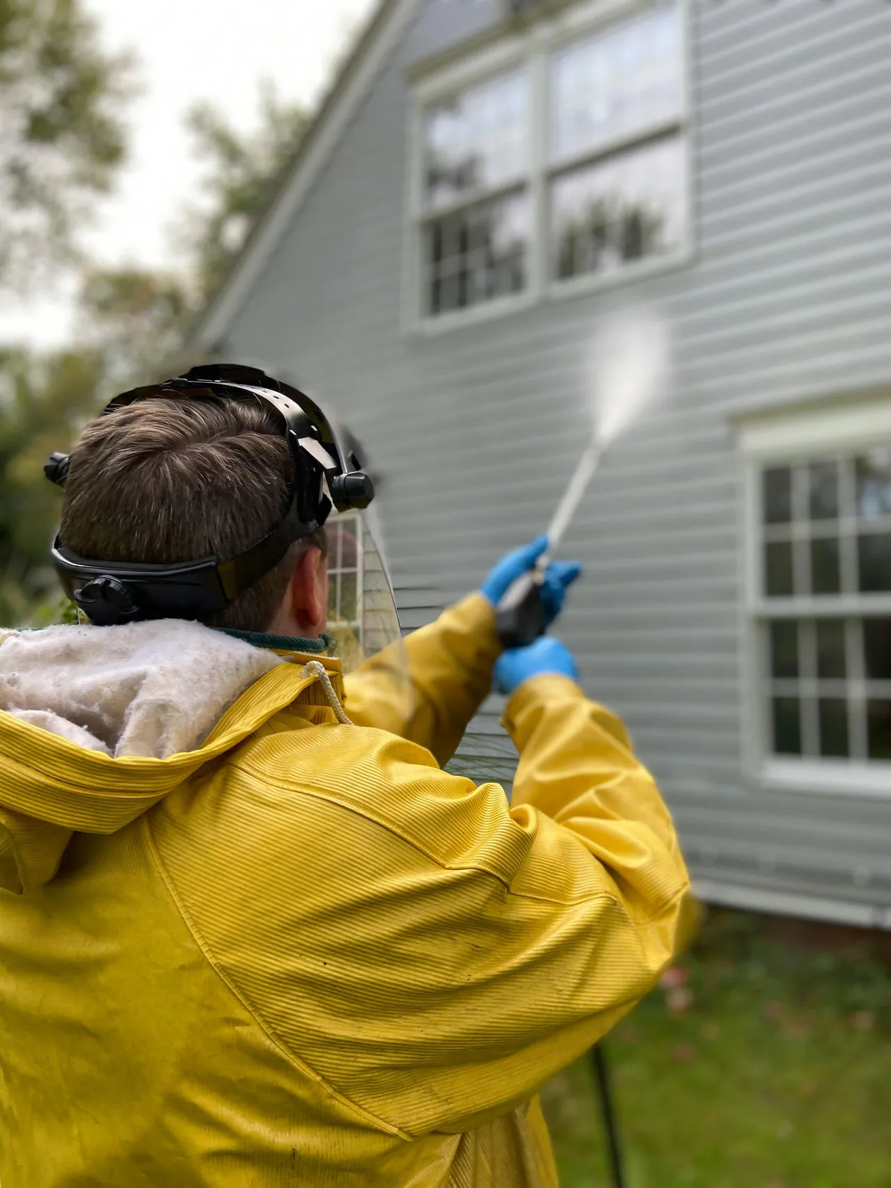 Person in yellow raincoat pressure washing a house.
