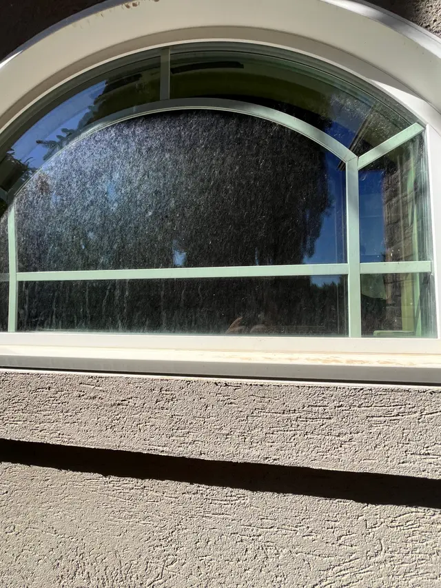 Arched window covered in white hard water streaks and mineral spots from sprinkler overspray on a Boise home