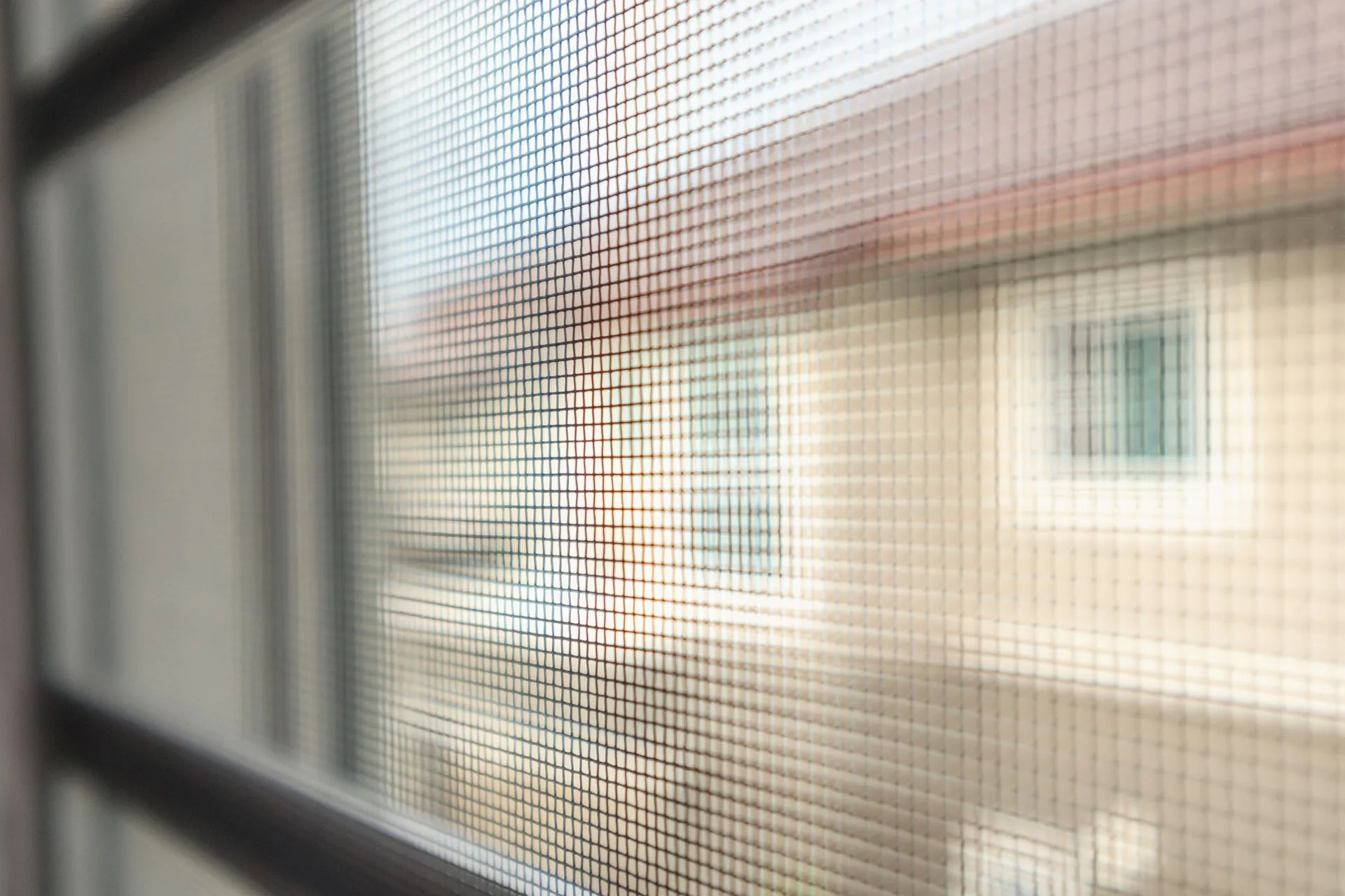Close-up view of a window screen, with a blurred outdoor scene of a building visible through it.
