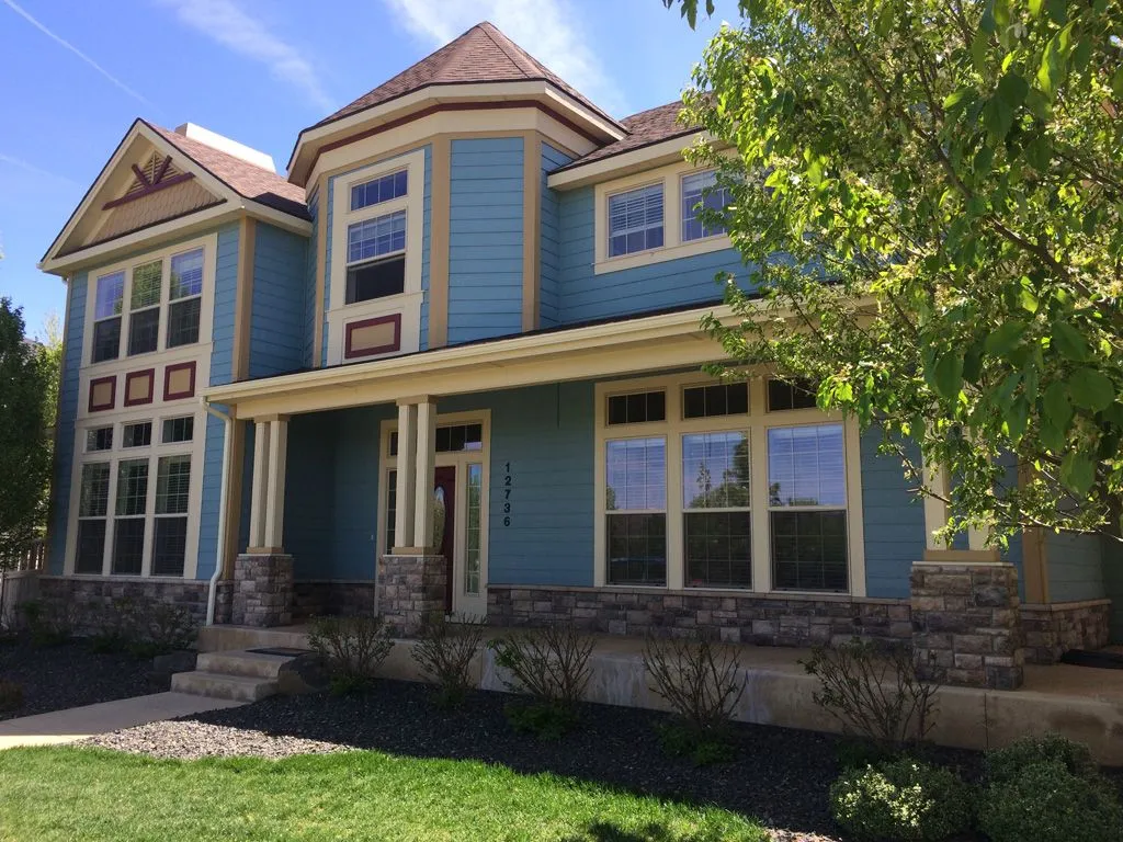 Blue two-story house with stone accents, windows, and porch under a bright sky.