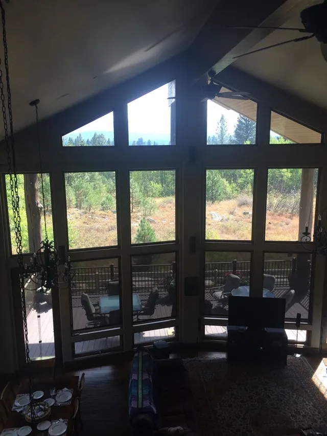A-framed room with large windows overlooking a forest and deck. Sunlight streams in.