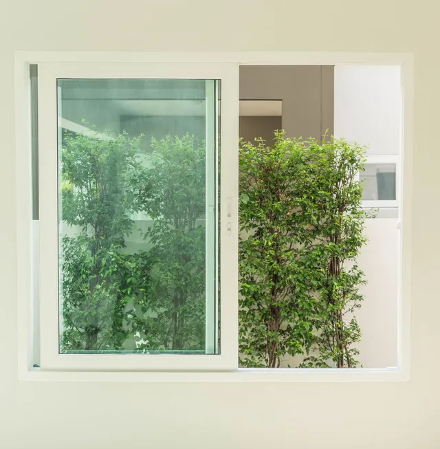 White sliding window with view of green trees and bushes outside.