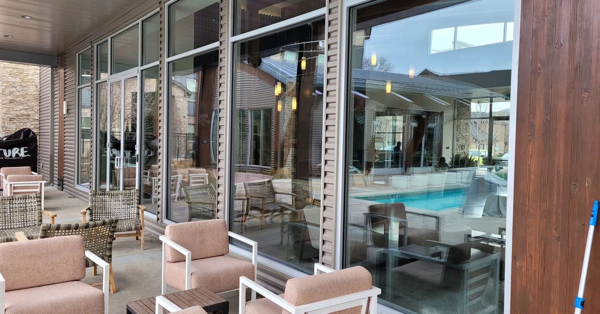 Outdoor patio with seating and large glass windows reflecting a pool and surrounding building.